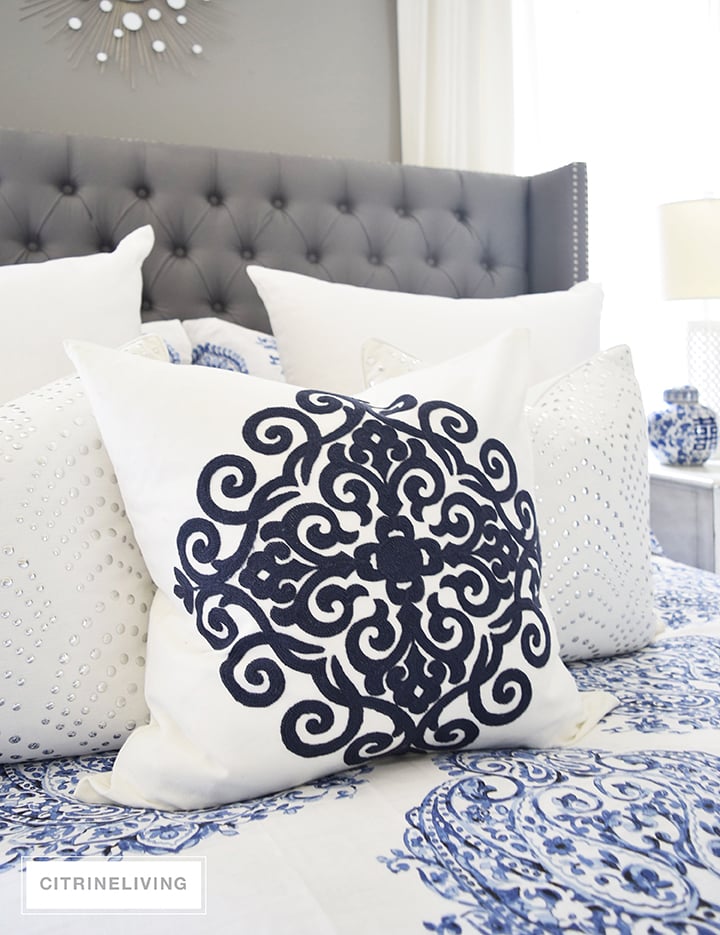 Master bedroom with gorgeous blue and white bedding, grey upholstered bed and white drapes.