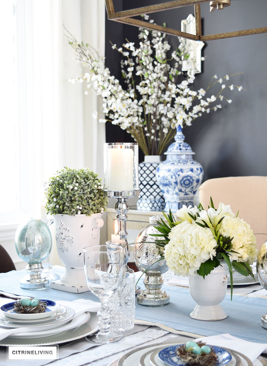 A gorgeous Easter tablescape with mercury glass accents and a mix of silver and white with blue and white china. Fresh and beautiful white hydrangeas are the perfect centerpiece.