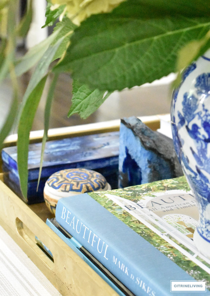 Summer decorated living with layers of beautiful blue patterned pillows, accented with fresh hydrangeas and greenery arranged in a blue an white ginger jar. Blue accessories and coastal elements enhance the Summer theme. 