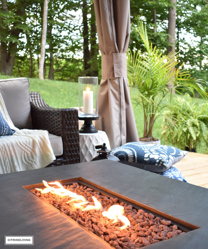 Create the perfect lounging area in your backyard with a beautiful covered gazebo, with added height for an airy, open feel. A gorgeous fire table to keep warm on chilly nights, solar chandelier, resin wicker furniture, and layered accessories create an elegant and sophisticated look.