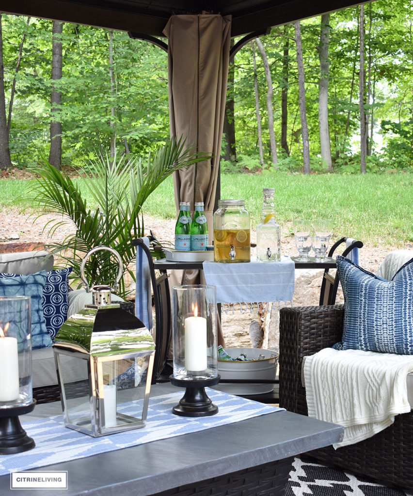 Create the perfect lounging area in your backyard with a beautiful covered gazebo, with added height for an airy, open feel. A gorgeous fire table, solar chandelier, resin wicker furniture, bar cart and layered accessories create an elegant and sophisticated look.