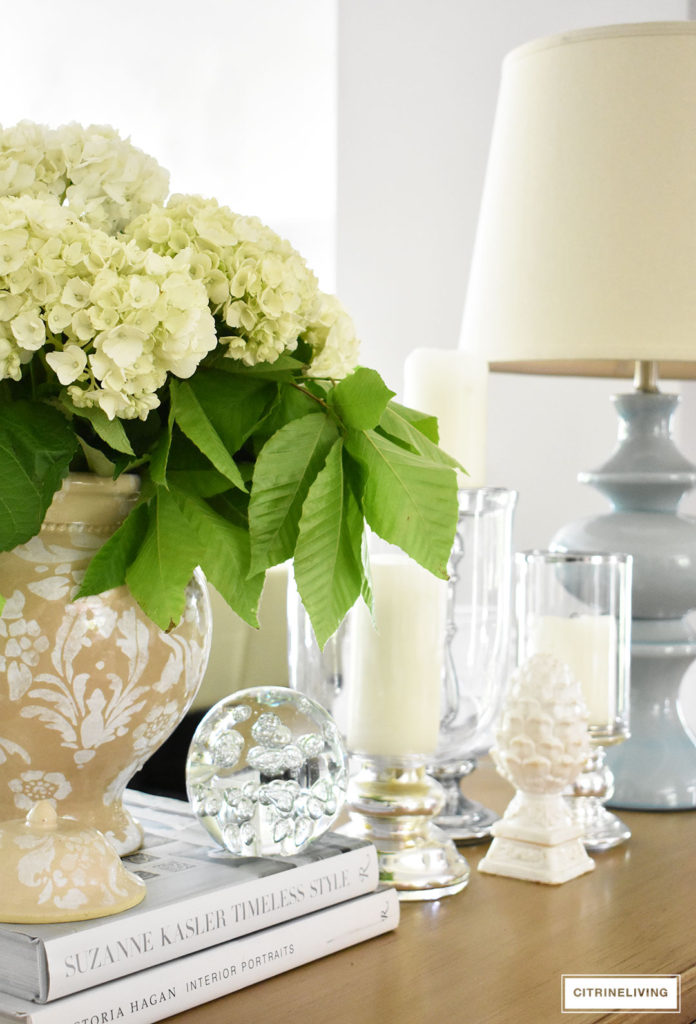 Fresh hydrangeas arranged in a classic ginger jar paired with glass hurricanes is the perfect touch of Summer decor in any room.