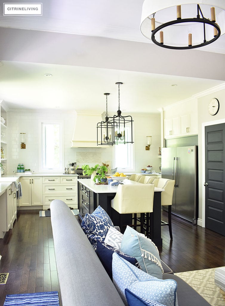 White kitchen with black island decorated for Summer with fresh cute greenery and bowls filled with bright, seasonal fresh fruit for a vibrant punch of seasonal color. Blue and white dishes and bowls are a classic touch.