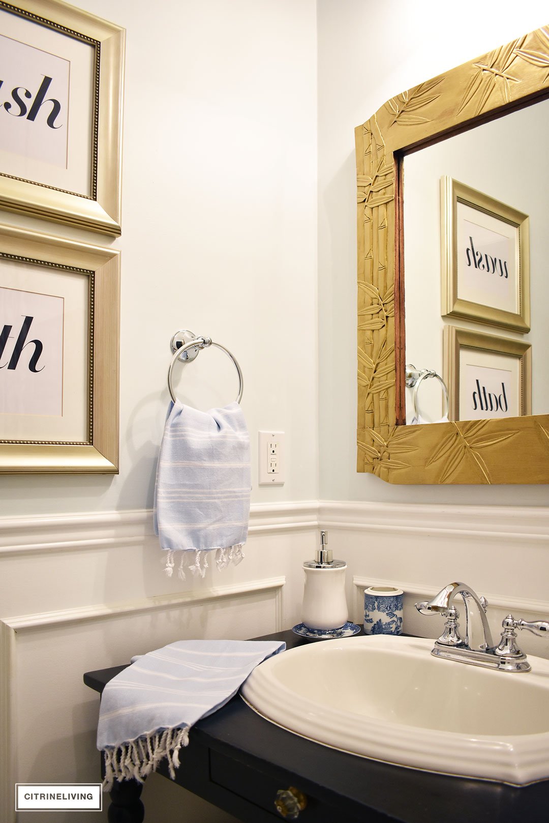 Small bathroom with white wainscotting, light blue walls, black vanity and gold accents.