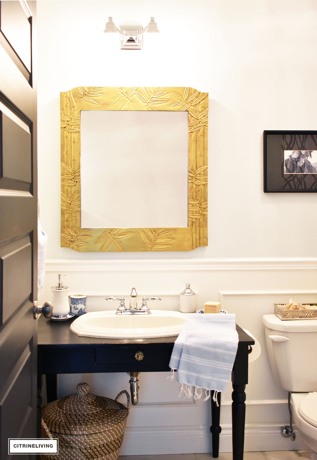 Small bathroom with white wainscotting, light blue walls, black vanity and gold accents.