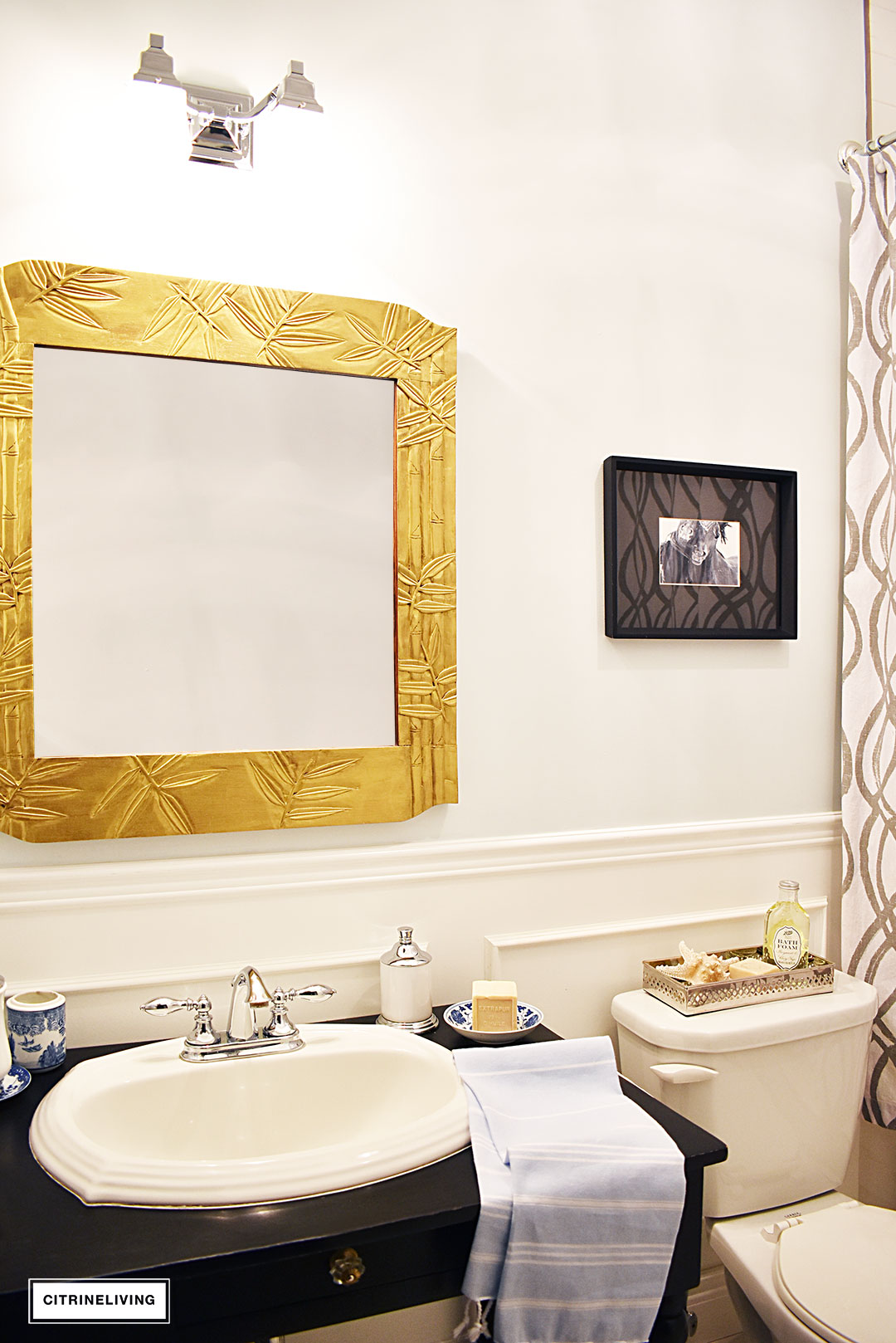 Small bathroom with white wainscotting, light blue walls, black vanity and gold accents.