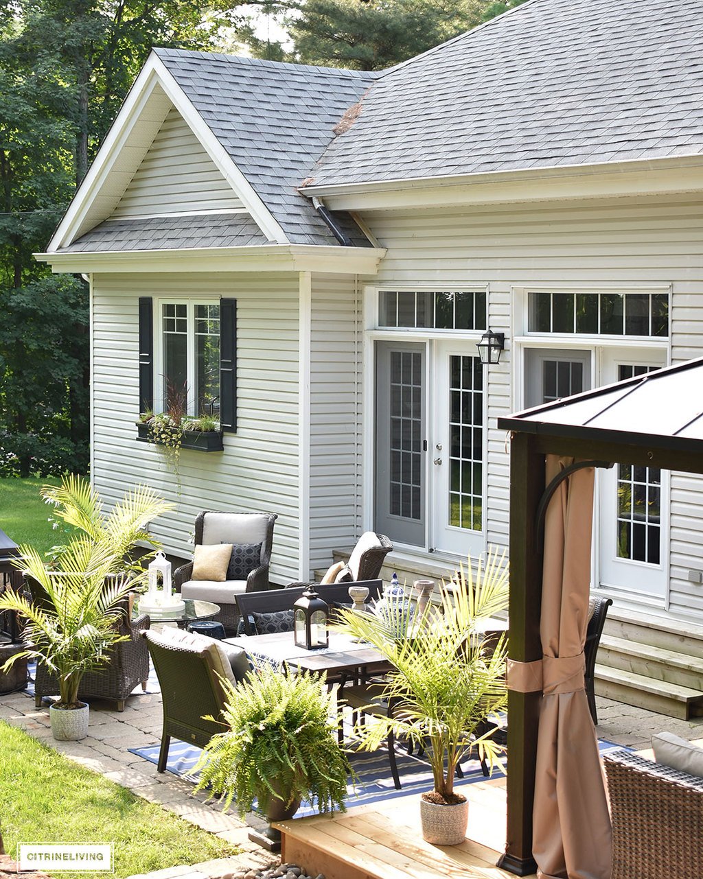 Home exterior with grey siding and roof, black shutters and window boxes, and backyard patio featuring 3 entertaining zones - lounge, dining and conversation.