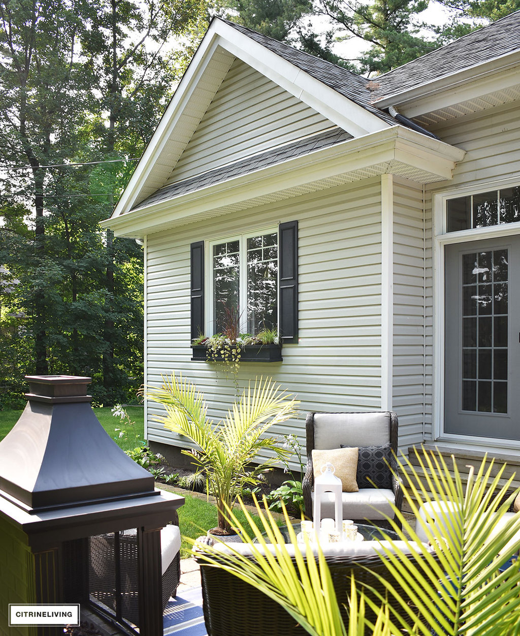 Home exterior with grey siding and roof, black shutters and window boxes, and backyard patio featuring 3 entertaining zones - lounge, dining and conversation.