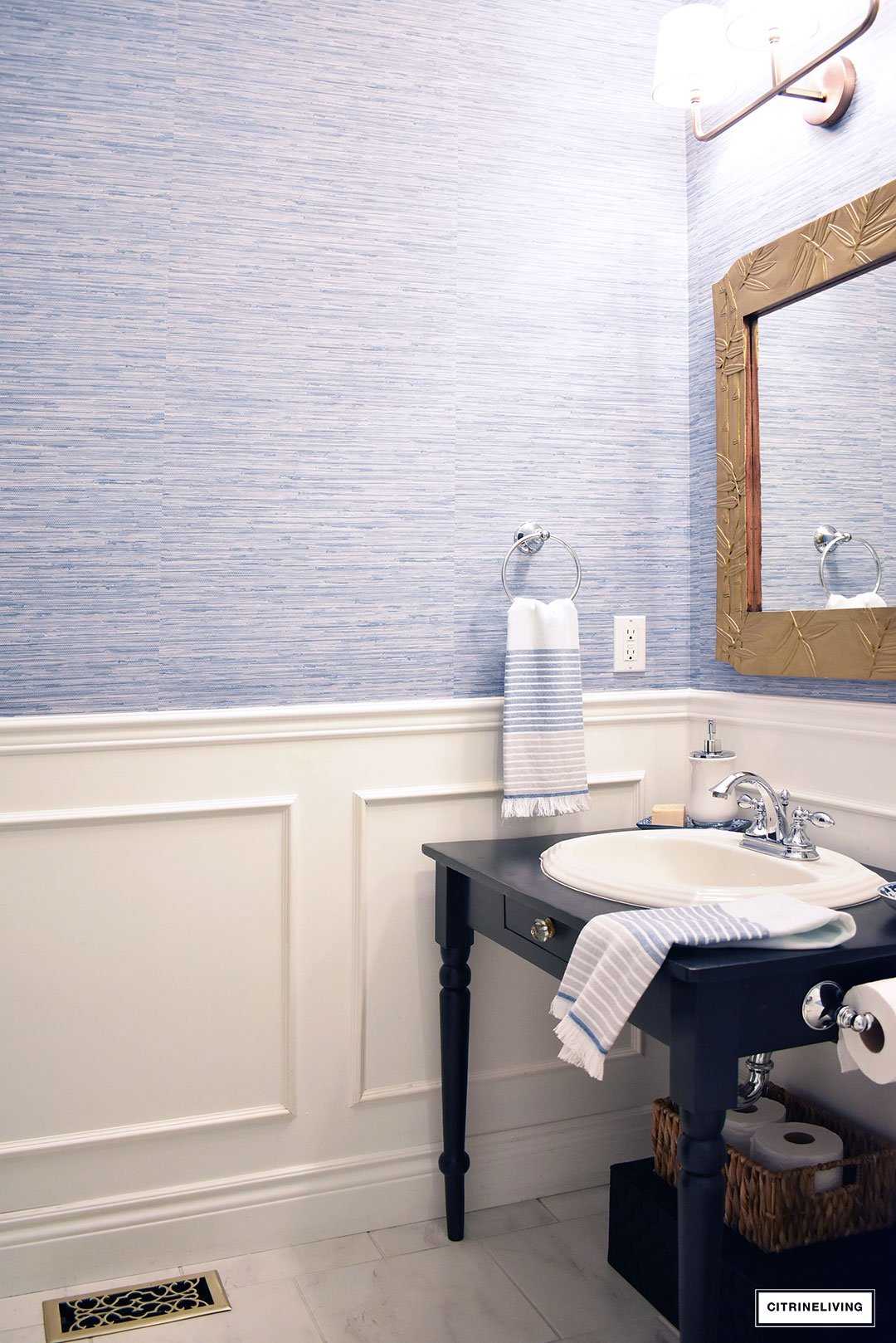 A timeless blue and white bathroom makeover featuring grasscloth, brass lighting, a blue and white striped shower curtain and blue and white accessories creates a sophisticated and elegant look in this small bath.