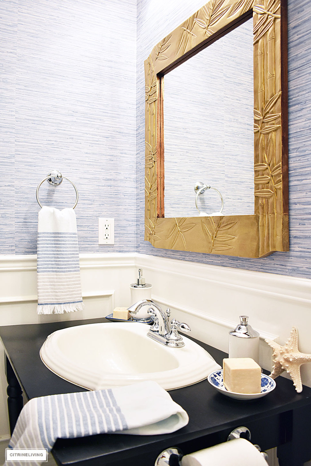 A timeless blue and white bathroom makeover featuring grasscloth, brass lighting, a blue and white striped shower curtain and blue and white accessories creates a sophisticated and elegant look in this small bath.