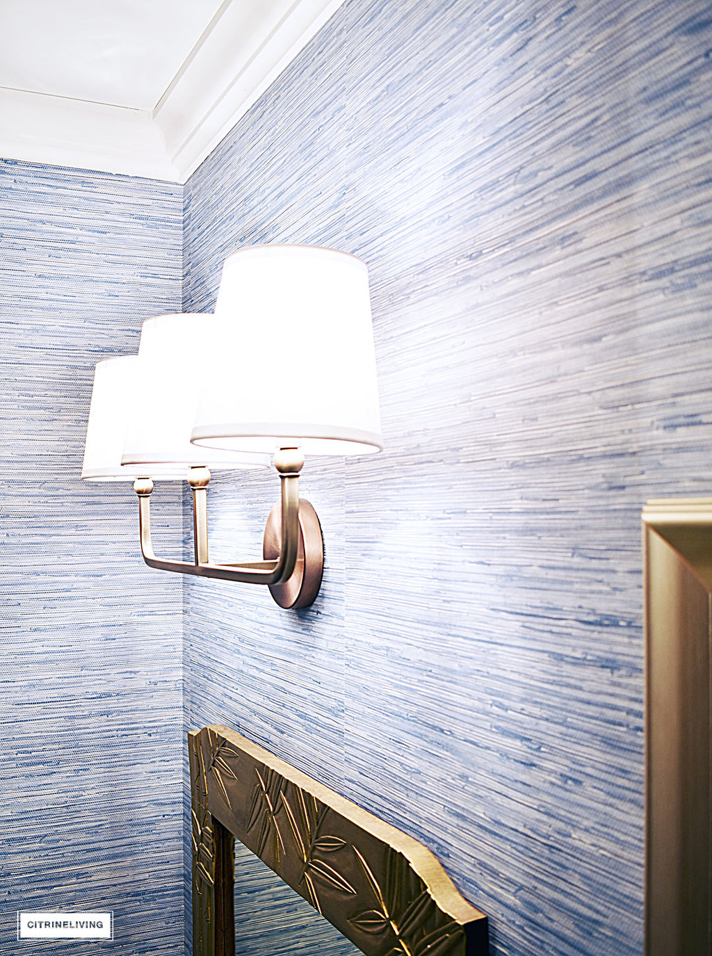A timeless blue and white bathroom makeover featuring grasscloth, brass lighting, a blue and white striped shower curtain and blue and white accessories creates a sophisticated and elegant look in this small bath.