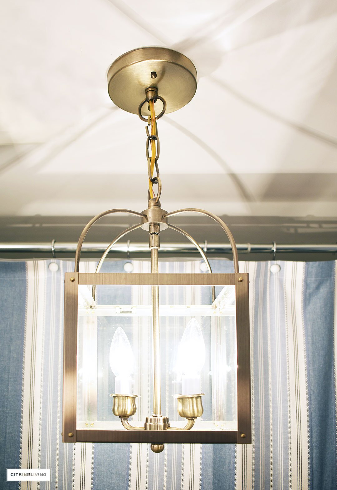 A timeless blue and white bathroom makeover featuring grasscloth, brass lighting, a blue and white striped shower curtain and blue and white accessories creates a sophisticated and elegant look in this small bath.