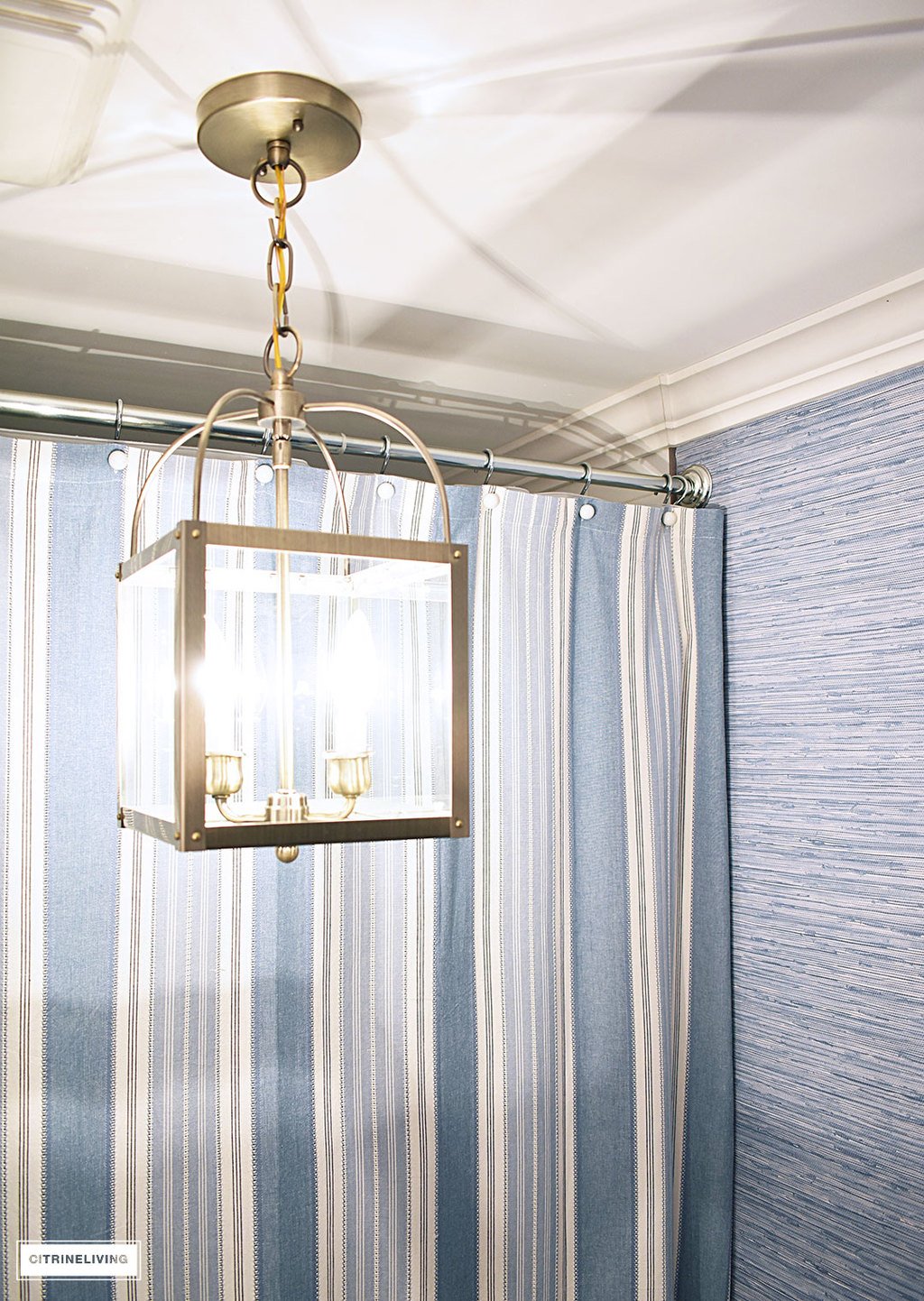 A timeless blue and white bathroom makeover featuring grasscloth, brass lighting, a blue and white striped shower curtain and blue and white accessories creates a sophisticated and elegant look in this small bath.