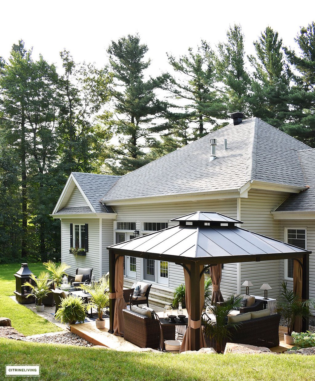 Home exterior with grey siding and roof, black shutters and window boxes, and backyard patio featuring 3 entertaining zones - lounge, dining and conversation.