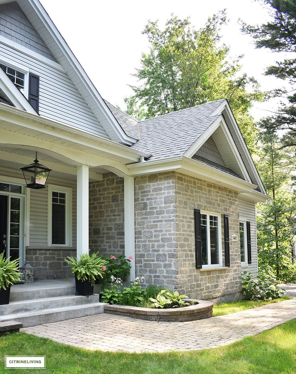 East coast style home featuring overscale black pendant porch light - Crestwood pendant by Progress Lighting - black front door, black shutters and two-tone grey siding and stone.