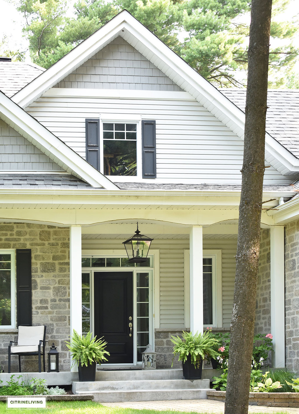 East coast style home featuring overscale black pendant porch light - Crestwood pendant by Progress Lighting - black front door, black shutters and two-tone grey siding and stone.