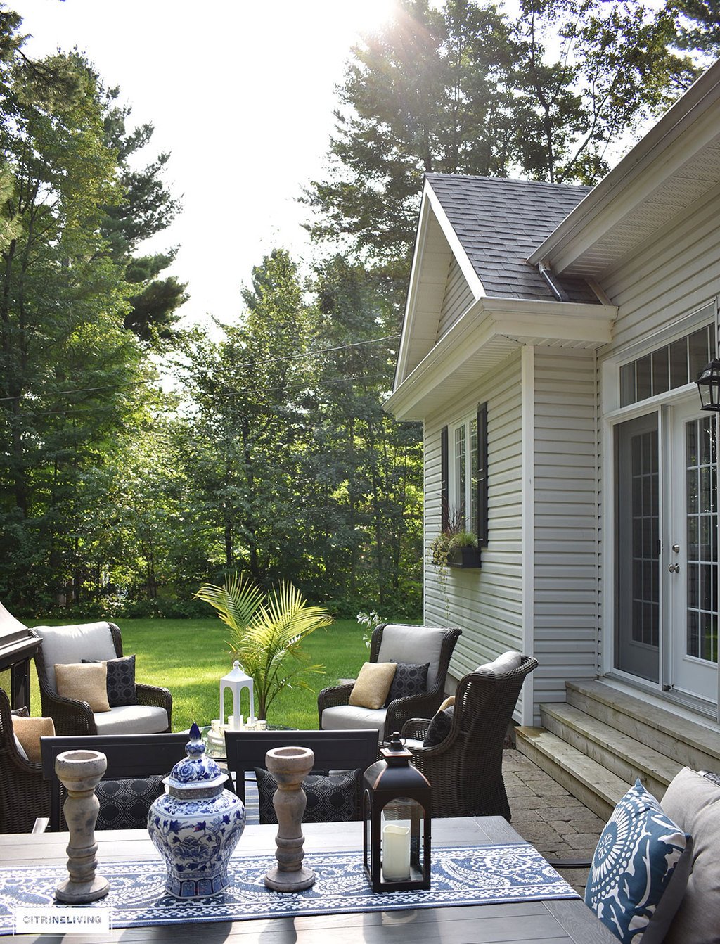 Home exterior with grey siding and roof, black shutters and window boxes, and backyard patio featuring 3 entertaining zones - lounge, dining and conversation.