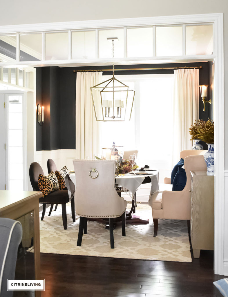 Fall Home Tour. Black dining room with elegant furniture. Leopard pillows. Brass overscale lantern style chandelier. Blue and white accents.