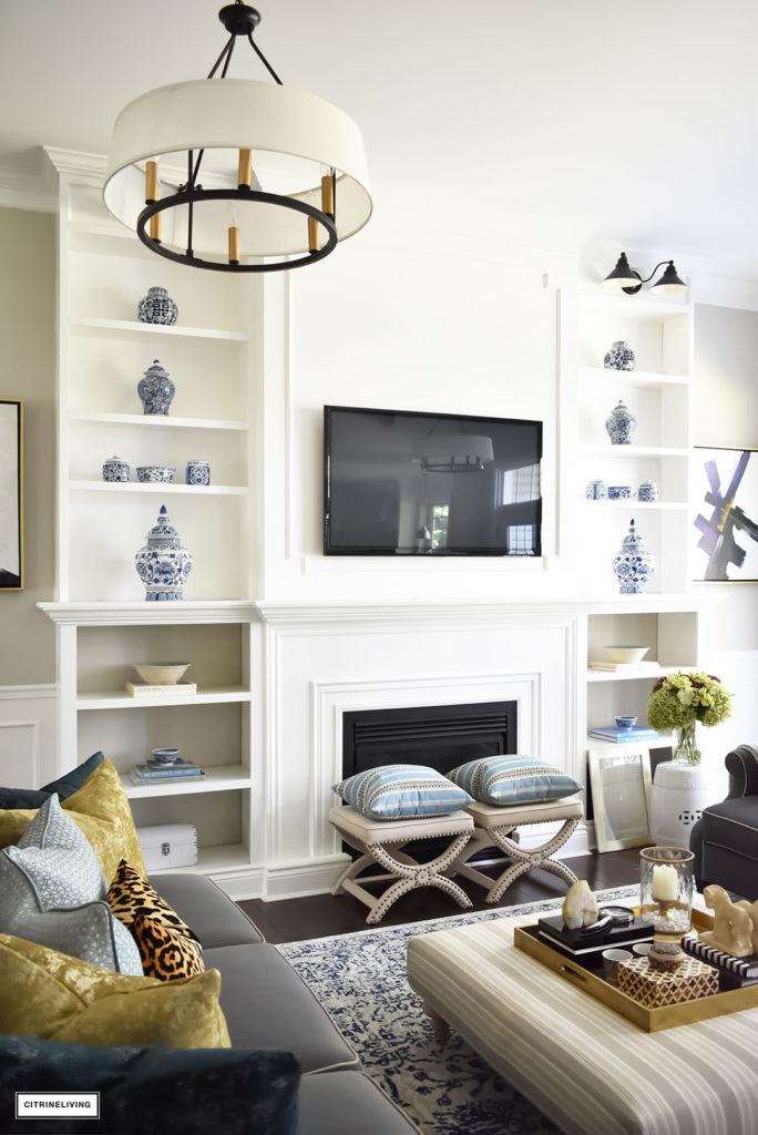 Fall Home Tour featuring this elegant living room with sophisticated navy and gold accents, drum shade chandeliers, gray sofas and blue and white accessories. Blue vintage style rug. Built in bookshelves.