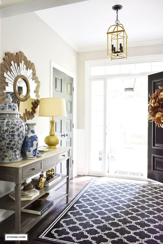 Fall home tour with elegant entryway featuring layers of gold accessories and blue and white ginger jars. Black and white quatrefoil rug. Two-toned brass and black pendant light