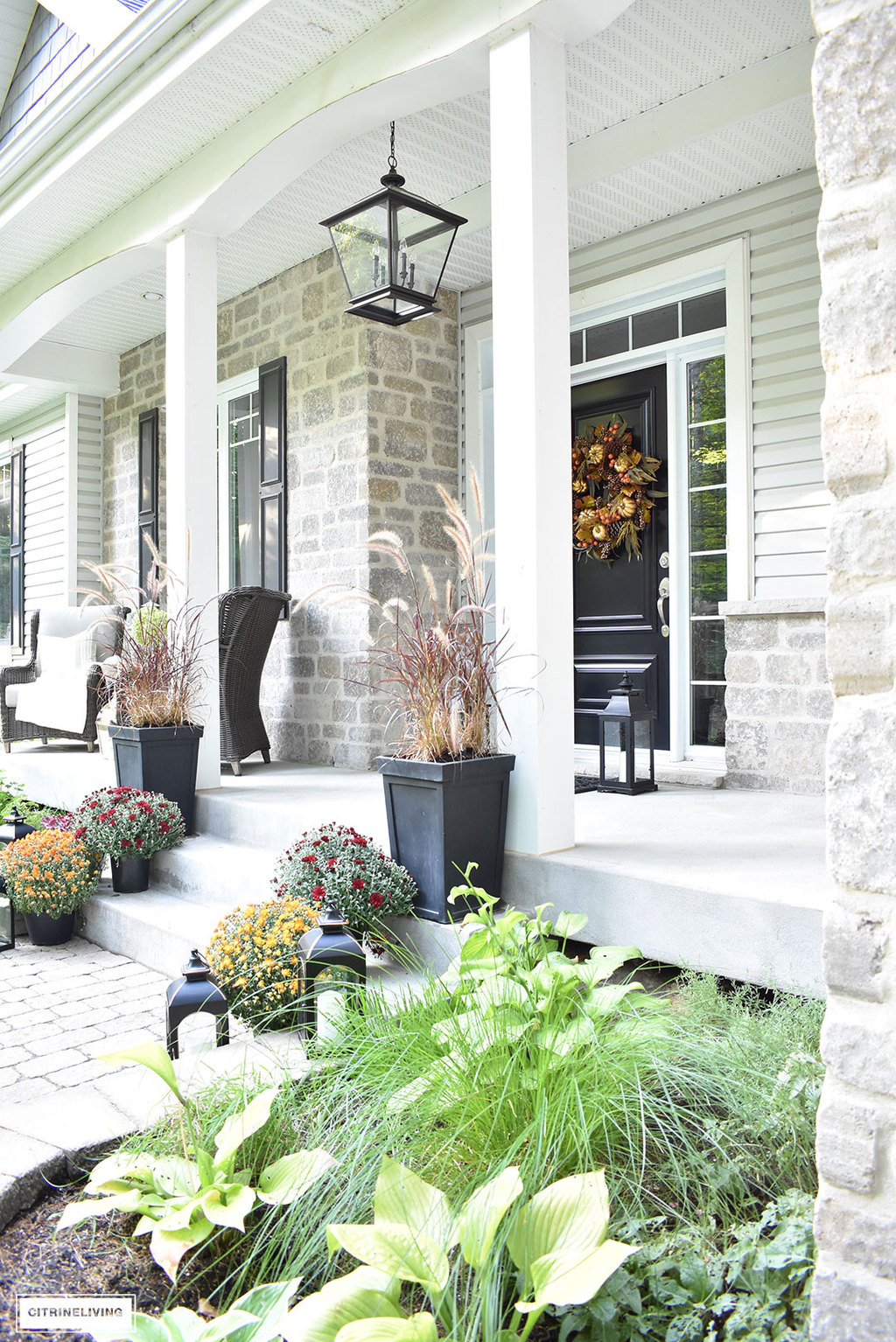 A simple and elegant front porch decorated for Fall with seasonal flowers in autumnal colors, and a sophisticated overscale wreath for the front door.