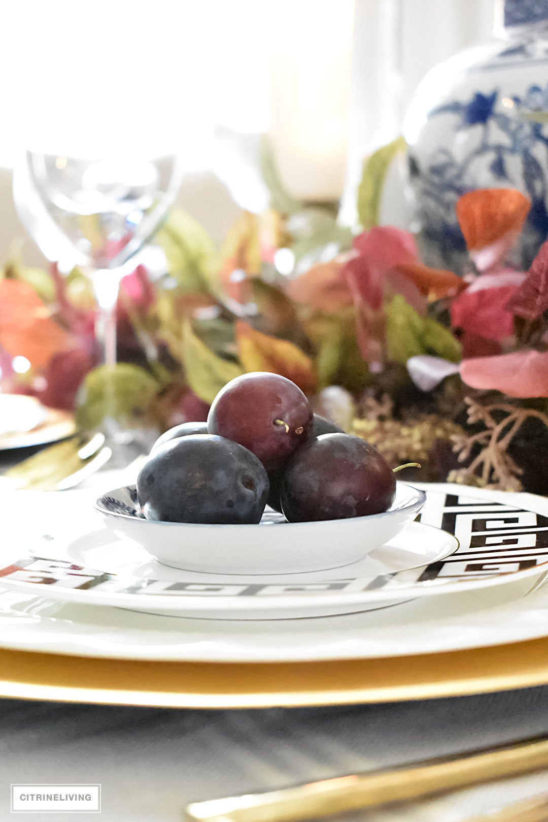 Create an elegant Fall tablescape using faux foliage in rich, autumnal hues, paired with gold, black and white tableware, and blue and white chinoiserie.