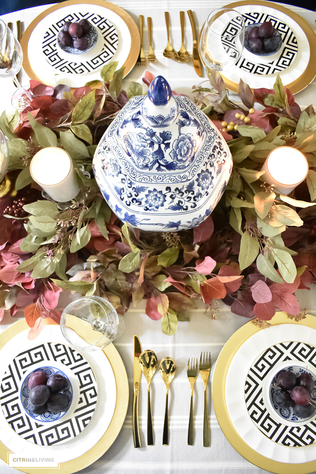 Create an elegant Fall tablescape using faux foliage in rich, autumnal hues, paired with gold, black and white tableware, and blue and white chinoiserie.
