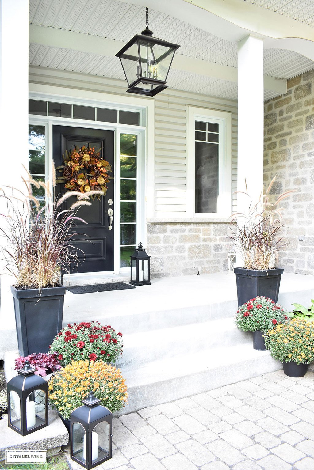 A simple and elegant front porch decorated for Fall with seasonal flowers in autumnal colors, and a sophisticated overscale wreath for the front door.