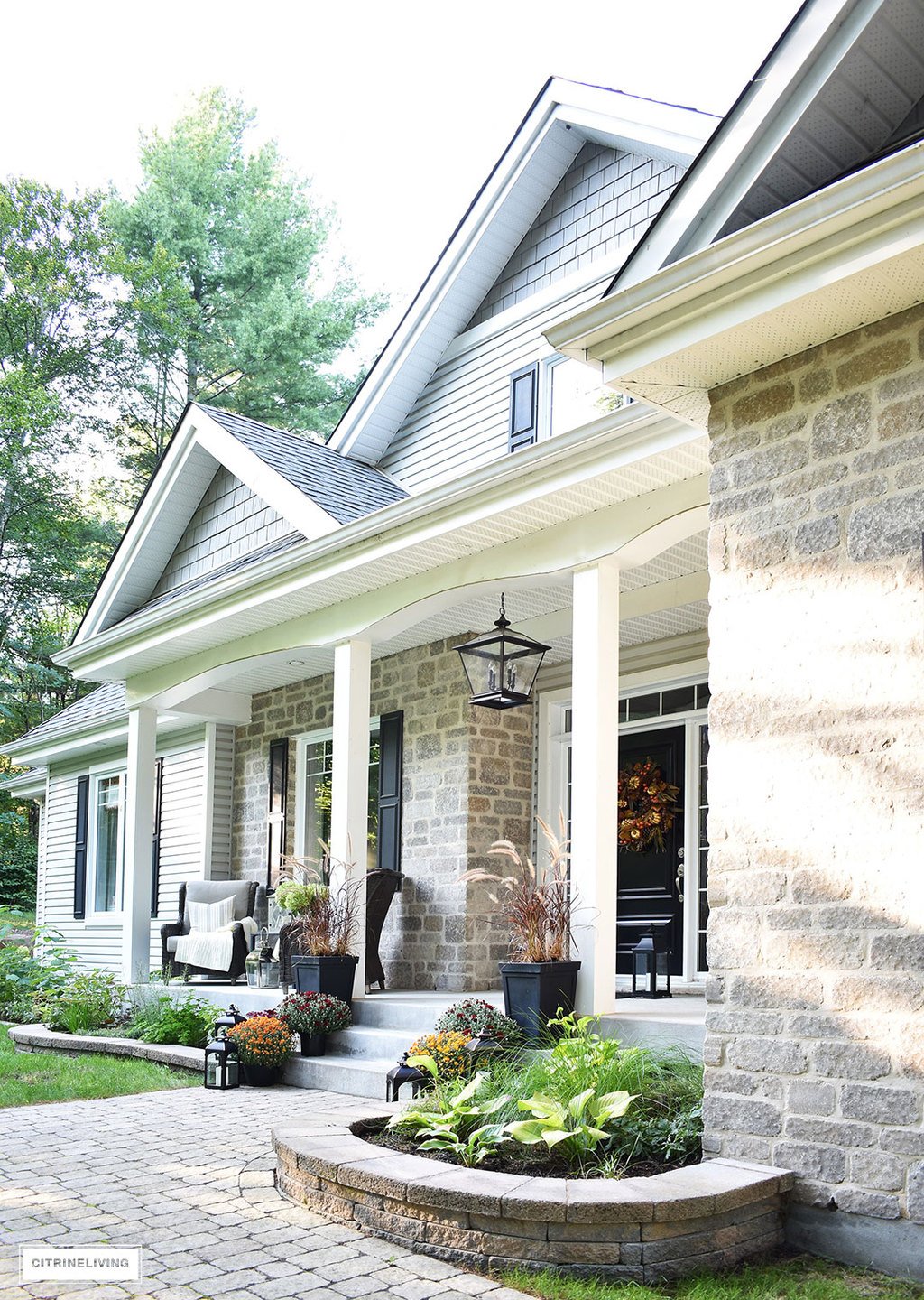 A simple and elegant front porch decorated for Fall with seasonal flowers in autumnal colors, and a sophisticated overscale wreath for the front door.