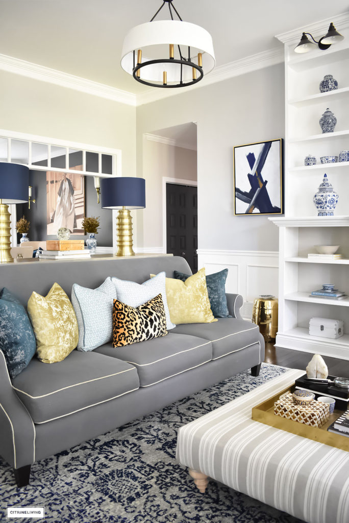 Fall Home Tour featuring this elegant living room with sophisticated navy and gold accents, drum shade chandeliers, gray sofas and blue and white accessories. Blue vintage style rug. Leopard pillow.