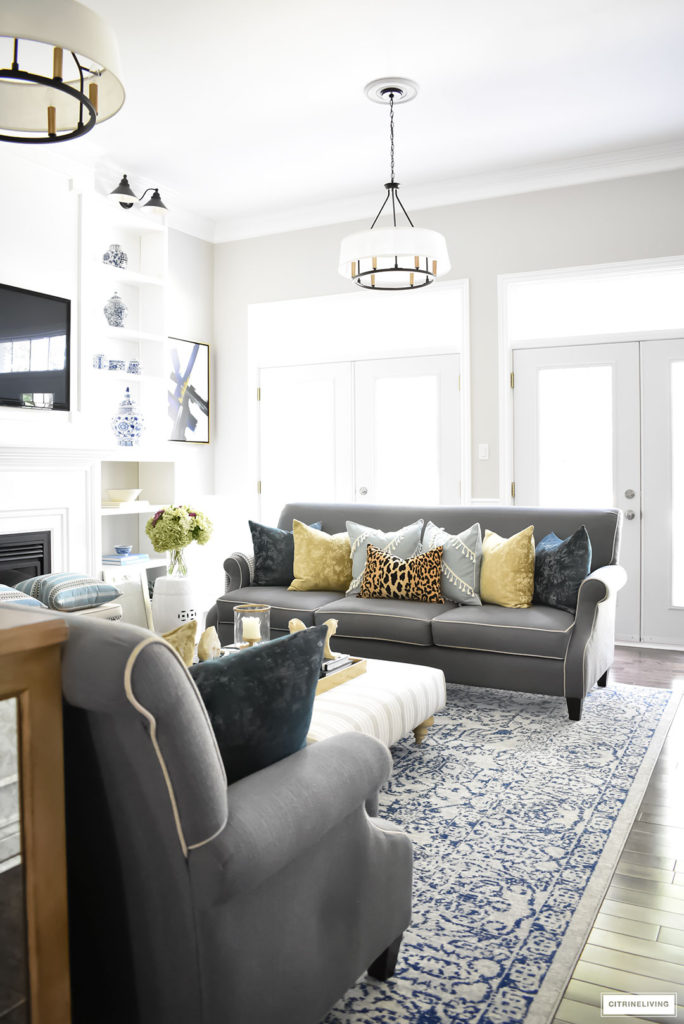 Fall Home Tour featuring this elegant living room with sophisticated navy and gold accents, drum shade chandeliers, gray sofas and blue and white accessories. Blue vintage style rug. Leopard pillow.