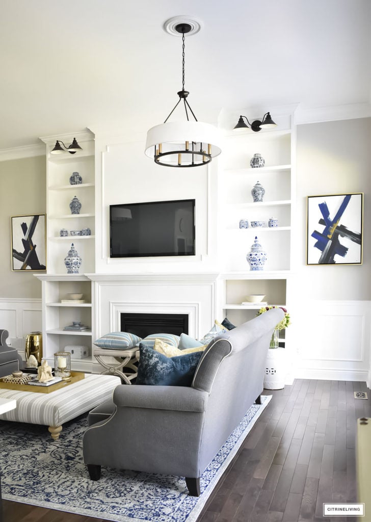 Fall Home Tour featuring this elegant living room with sophisticated navy and gold accents, drum shade chandeliers, gray sofas and blue and white accessories. Blue vintage style rug. Built in bookshelves.