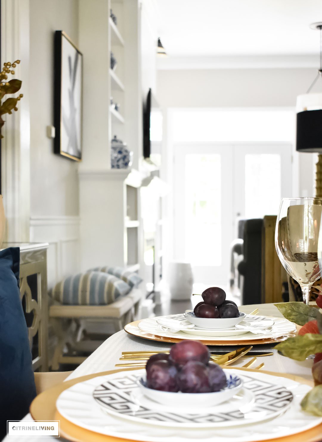 Create an elegant Fall tablescape using faux foliage in rich, autumnal hues, paired with gold, black and white tableware, and blue and white chinoiserie.