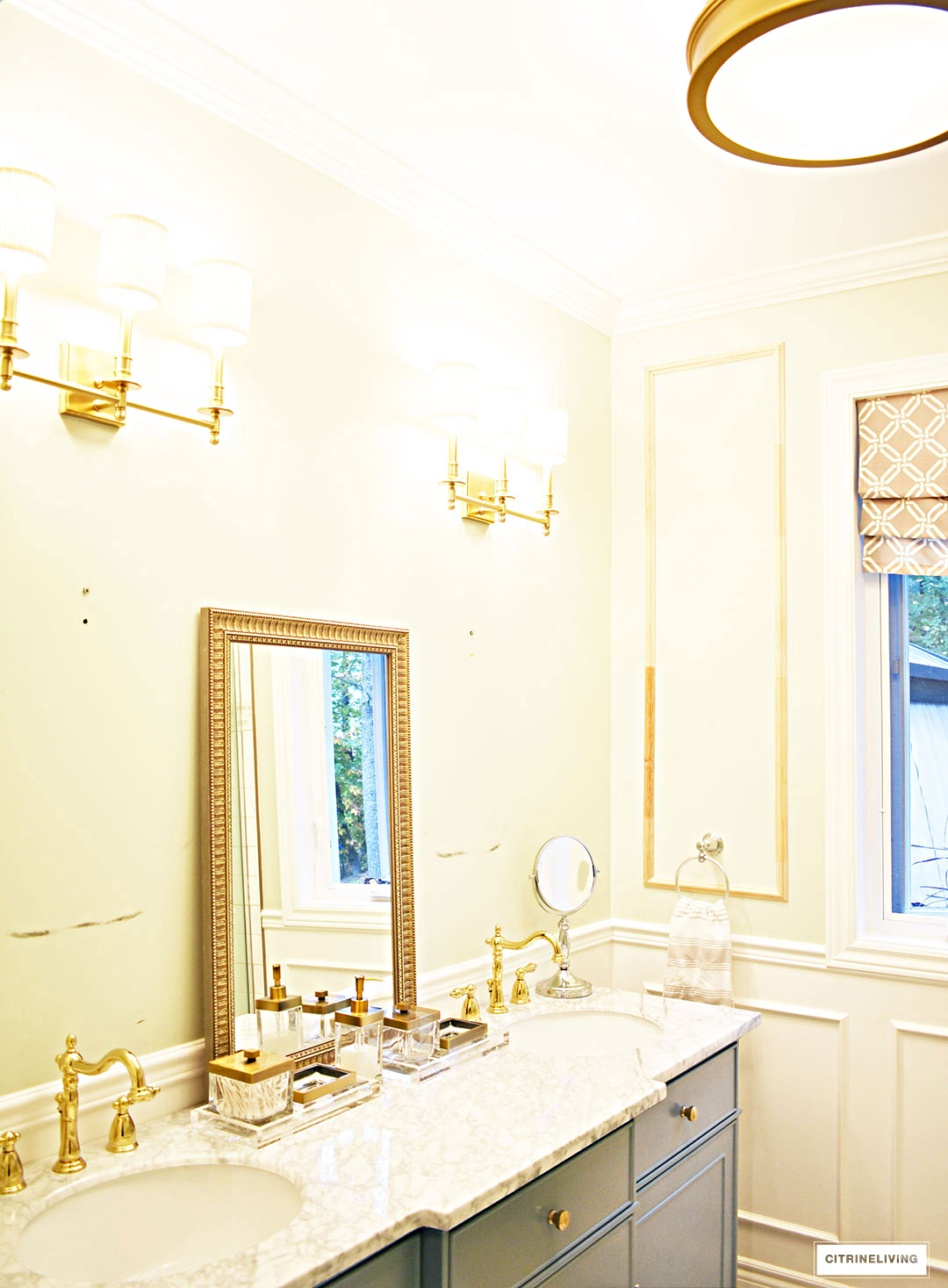 Gorgeous master bathroom makeover with wall panelling, brass lighting and a stunning gray vanity with marble counters.