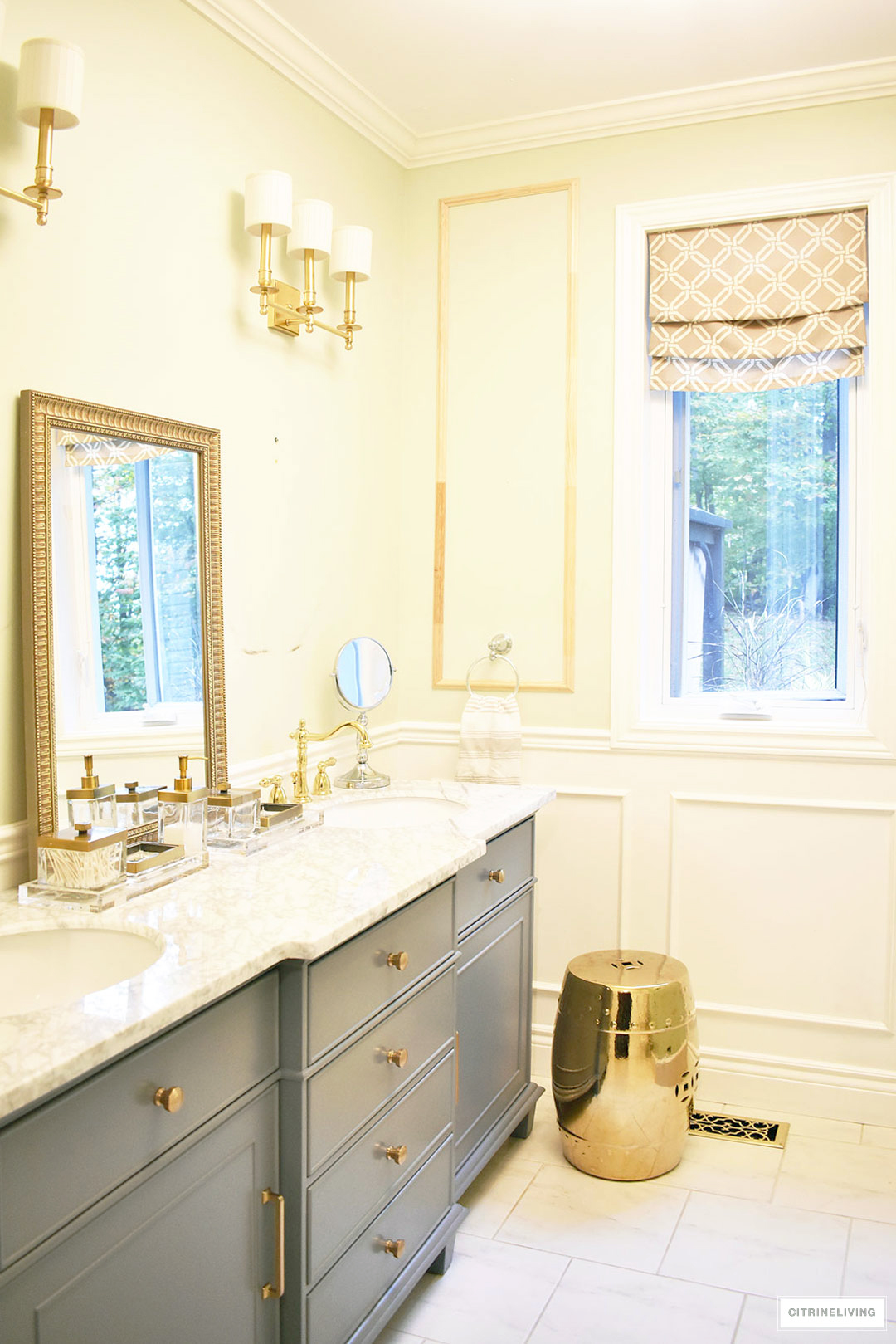 Gorgeous master bathroom makeover with wall panelling, brass lighting and a stunning gray vanity with marble counters.