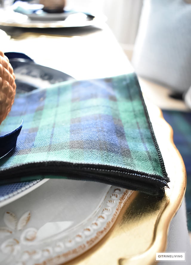 Gorgeous Christmas tablescape with classic navy and green tartan, accented with gold ornaments, chargers, flatware and glassware.