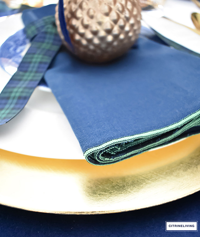 Gorgeous Christmas tablescape with classic navy and green tartan, accented with gold ornaments, chargers, flatware and glassware.