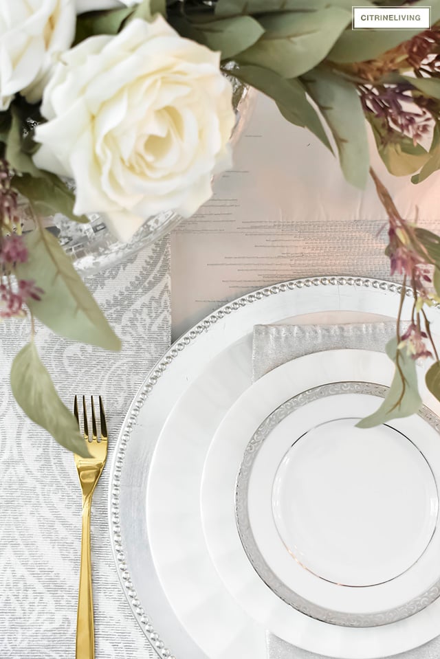 A gorgeous neutral Valentine's table with tones of white layered with metallic accents and a beautiful white rose centrepiece.