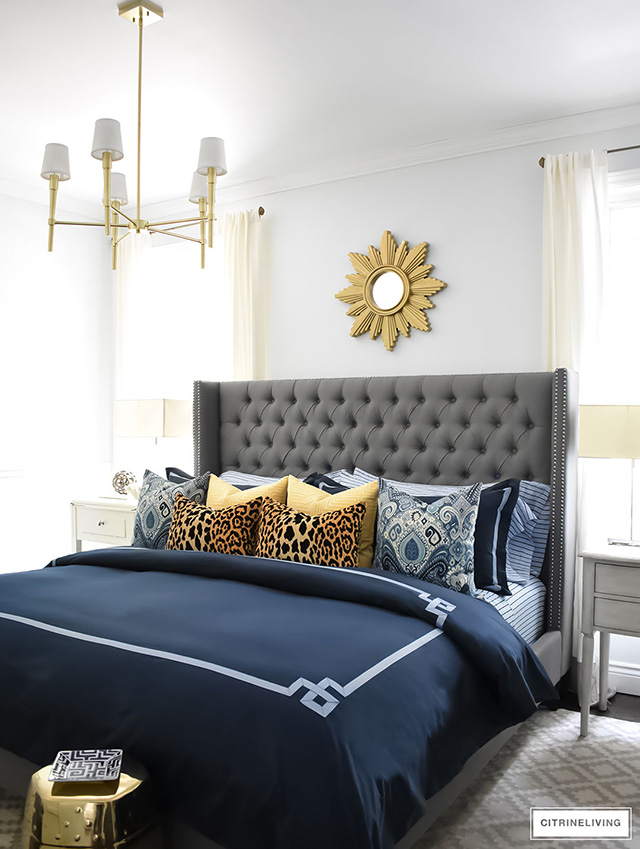 navy-bedding-grey-upholstered-heaboard-blue-and-white-pillows-gold-accents