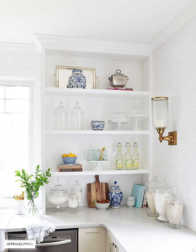 https://citrineliving.com/wp-content/uploads/2018/02/white-kitchen-open-shelves-blue-and-white-accessories-cookbook-cakestand-apothecary-jar-wall-sconce-1.jpg
