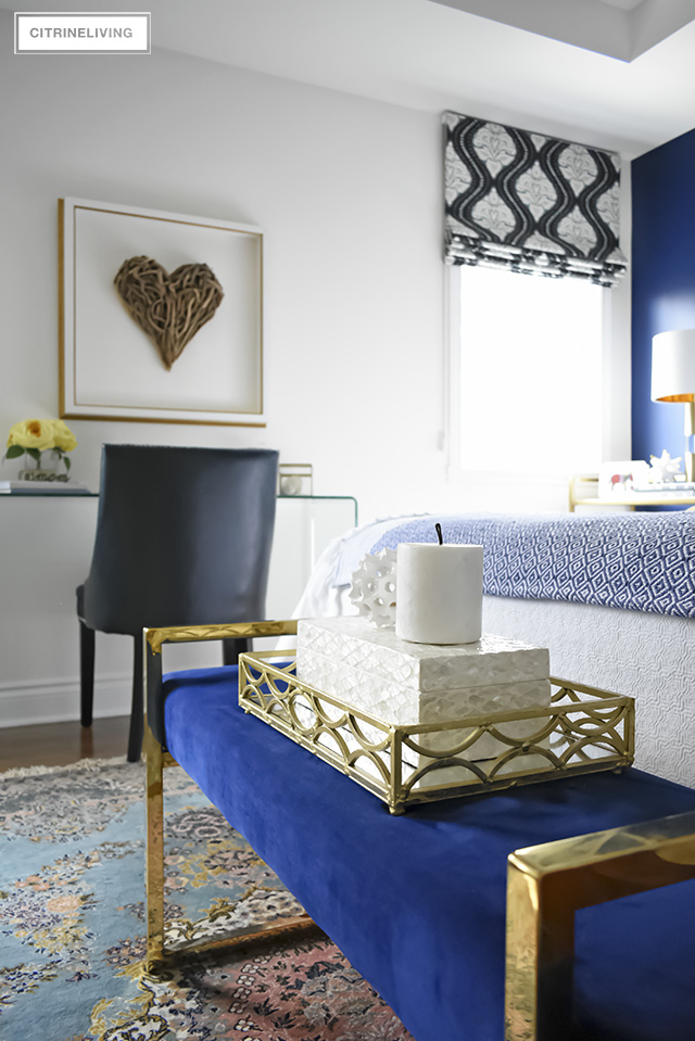 A beautiful blue velvet bench with brass tray and layers of white and cream accessories.