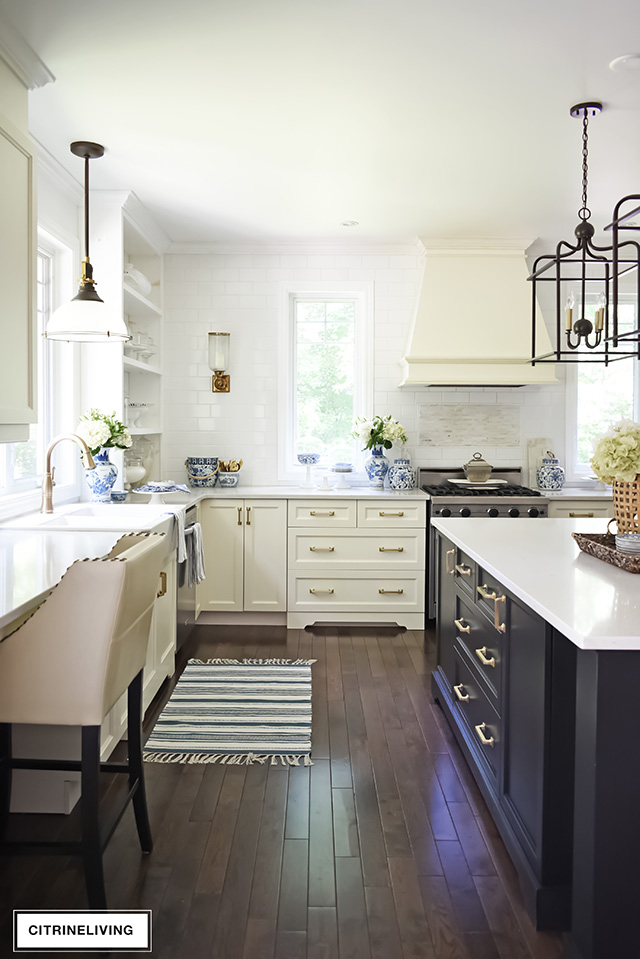 Traditional kitchen with ivory perimeter cabinets, black island with brass hardware, and counter to ceiling subway tile wall.