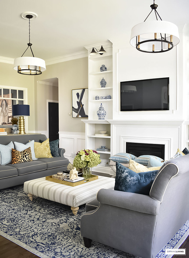 Living room with large builtin bookshelves, grey sofas, double chandeliers, blue vintage rug.
