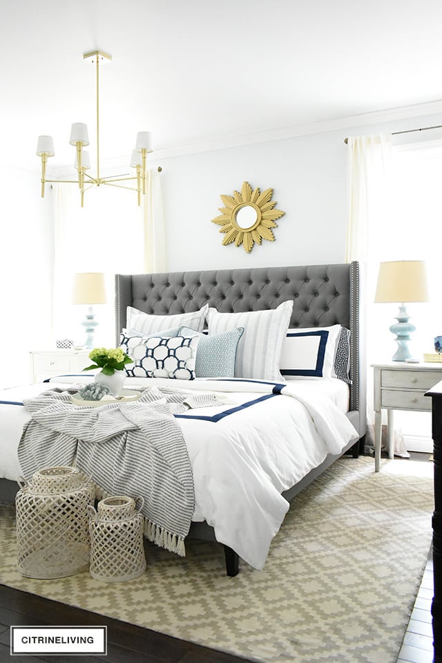 Coastal chic bedroom decor with layers of blue and white, woven accessories layered with striped pillows and throw blanket.