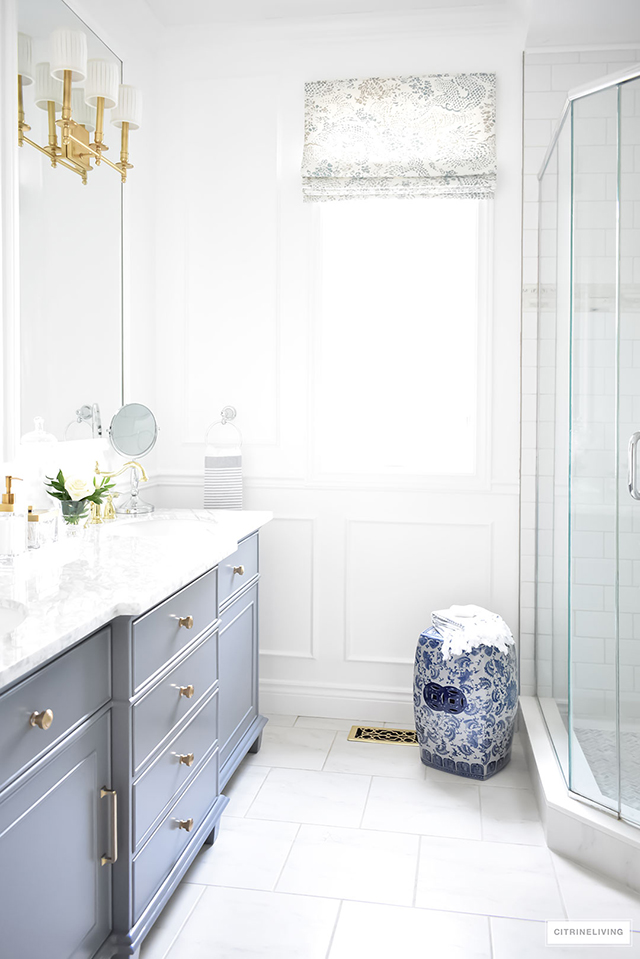 Favorite Makeovers! Master bathroom makeover with grey vanity, marble counters, brass lighting and accents. Blue and white garden stool.
