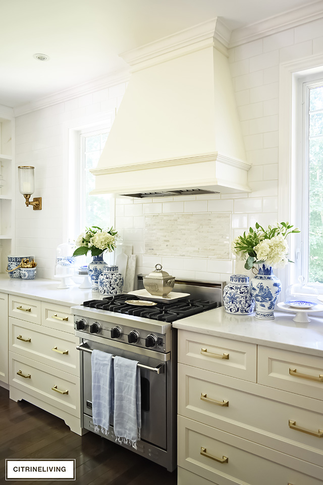 White kitchen with quartz countertops and brass hardware pulls, subway tile backsplash and no upper cabinets.