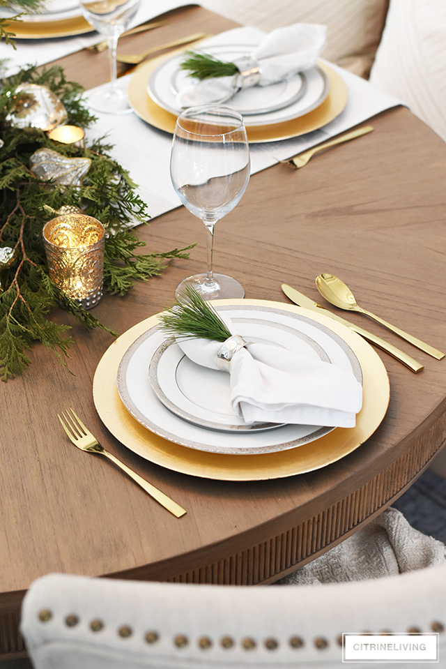Simple and elegant Christmas table with fresh greenery and ornaments, silver and gold china and flatware.