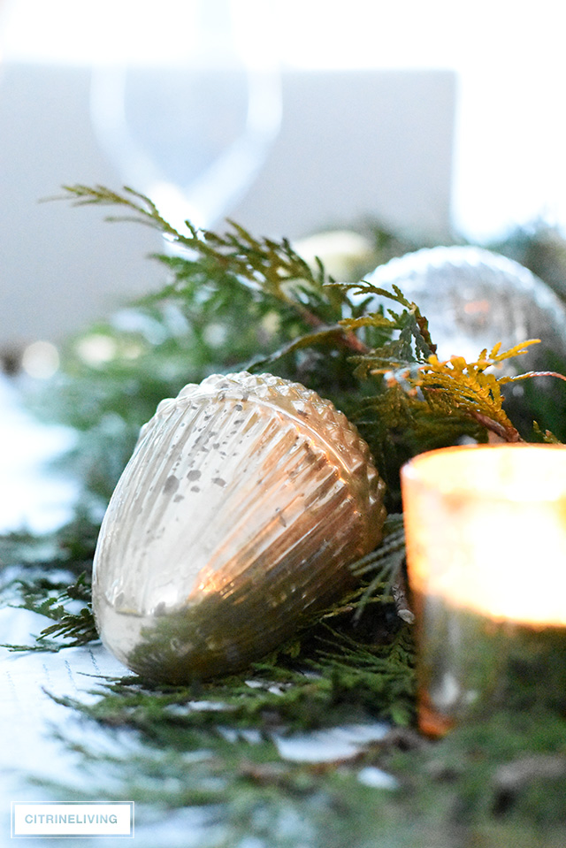 Christmas table with fresh greenery and beautiful ornaments - mercury glass acorn and votive candle.