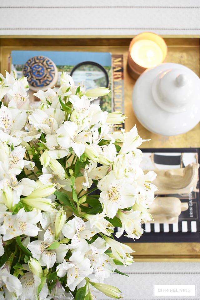 Living room styling ideas, this coffee table and ottoman vignette with oversized gold tray, design books and fresh florals.