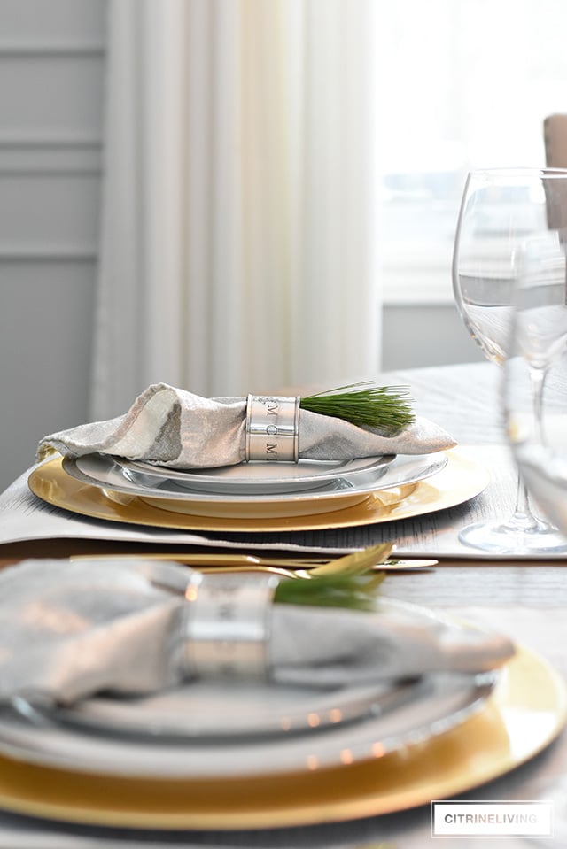 Simple and elegant Christmas table with fresh greenery and ornaments, silver and gold china and flatware.